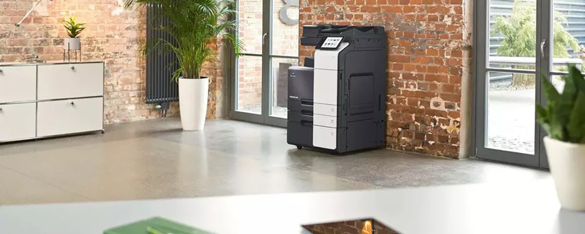 Fotocopiatrice moderna in ufficio dal design industriale con pareti in mattoni e piante verdi accanto alla porta a vetri